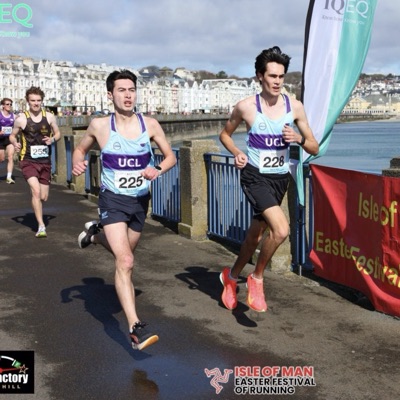Two UCL runners in the light blue club singlet racing along a seafront