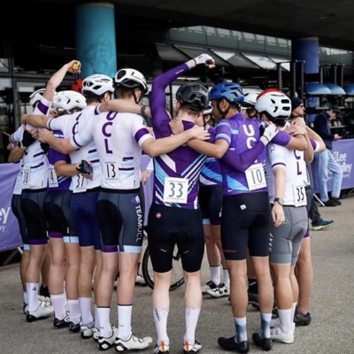 UCL riders in club kit in a huddle before a race, numbers pinned on