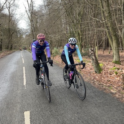 Two UCL riders in club kit riding a wet winter lane