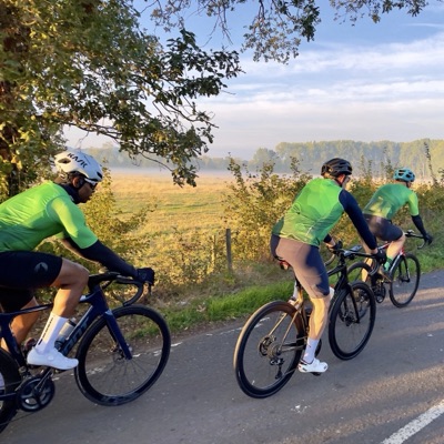 Three Dawn Raid Velo riders in the green kit passing a misty field